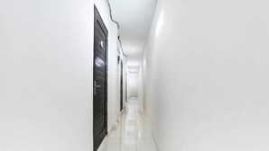 A narrow, well-lit hallway with white walls and a tiled floor, leading to a door at the end. - Akatara Stay Jimbaran (Jimbaran)