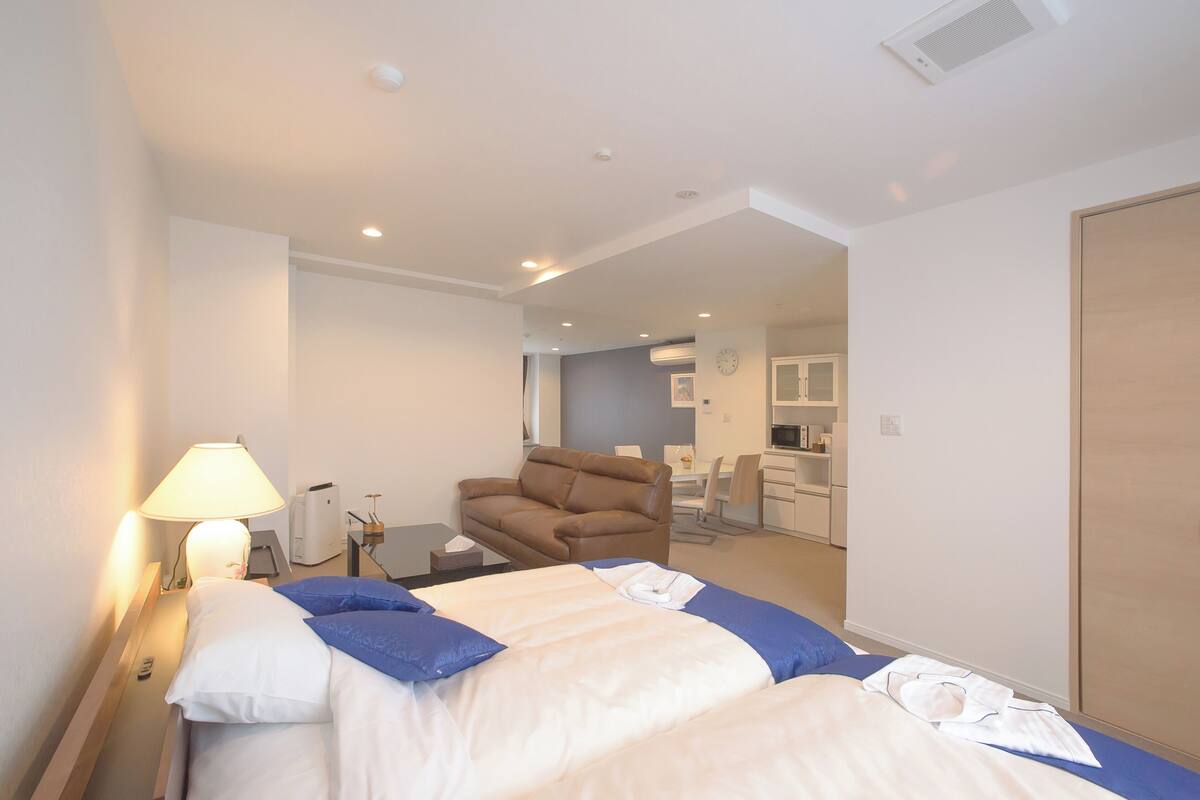 Habitación de hotel con cama, escritorio, silla y un espacio con kitchenette.