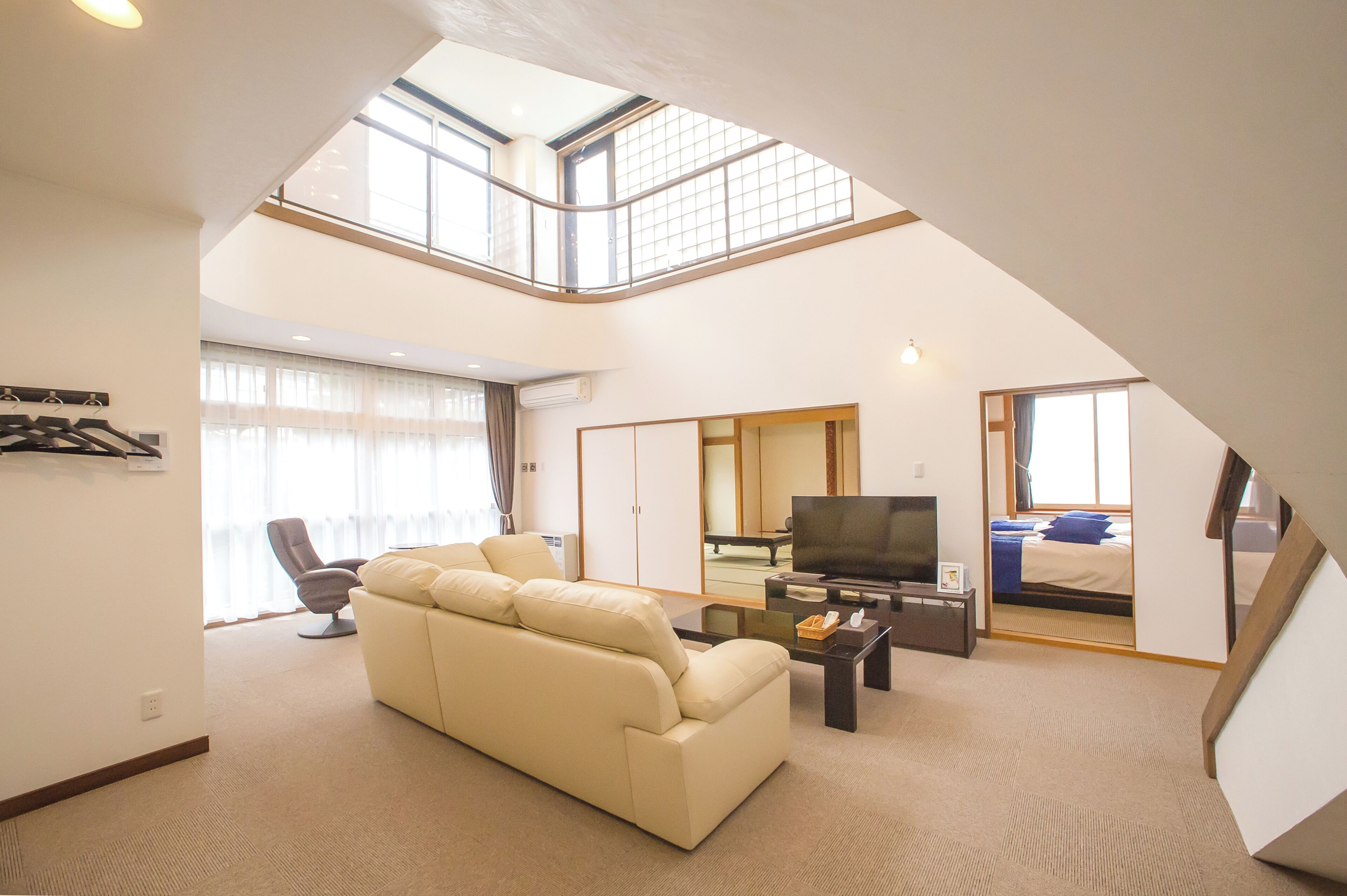 A high-ceiling living room with a sofa, TV, and a dining area.