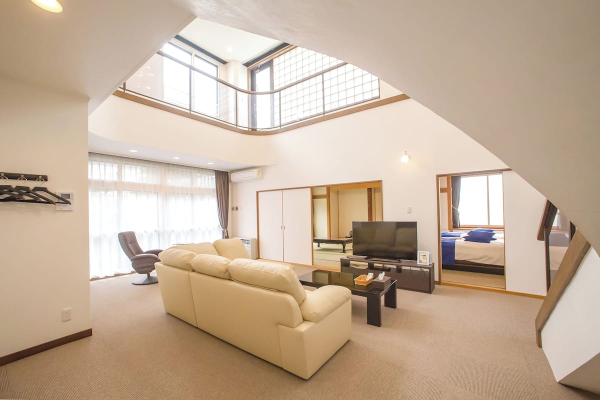 Ein Wohnzimmer mit hohen Decken, einer Couch, einem Fernseher und einem Essbereich.