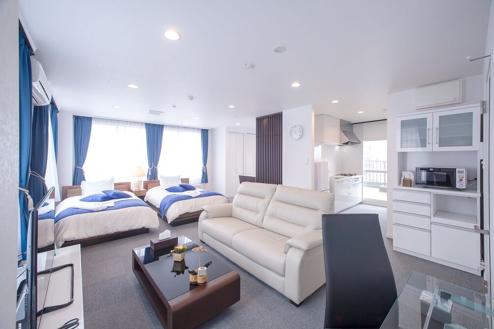 A hotel room with two beds, a sofa, a desk, a chair, a TV, a microwave, and a clock on the wall.
