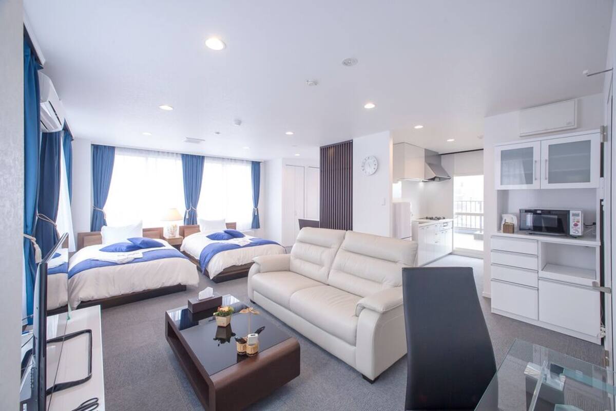 Habitación de hotel con dos camas, un sofá, un escritorio, una silla, un televisor, un microondas y un reloj en la pared.