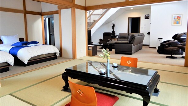 A traditional Japanese-style room with tatami flooring, a low table with a glass top, and a bed with a blue and white bedding. - Condominium Panoramique Motomachi (Hakodate)