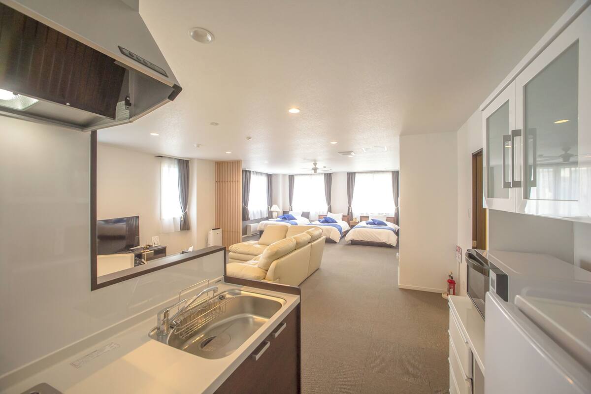 Habitación de hotel con kitchenette, un sofá, dos camas, un espejo grande y vistas al exterior.