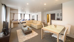 A modern hotel room with a living area, a dining table, a sofa, a TV, and a kitchen area. - Condominium Panoramique Motomachi (Hakodate)
