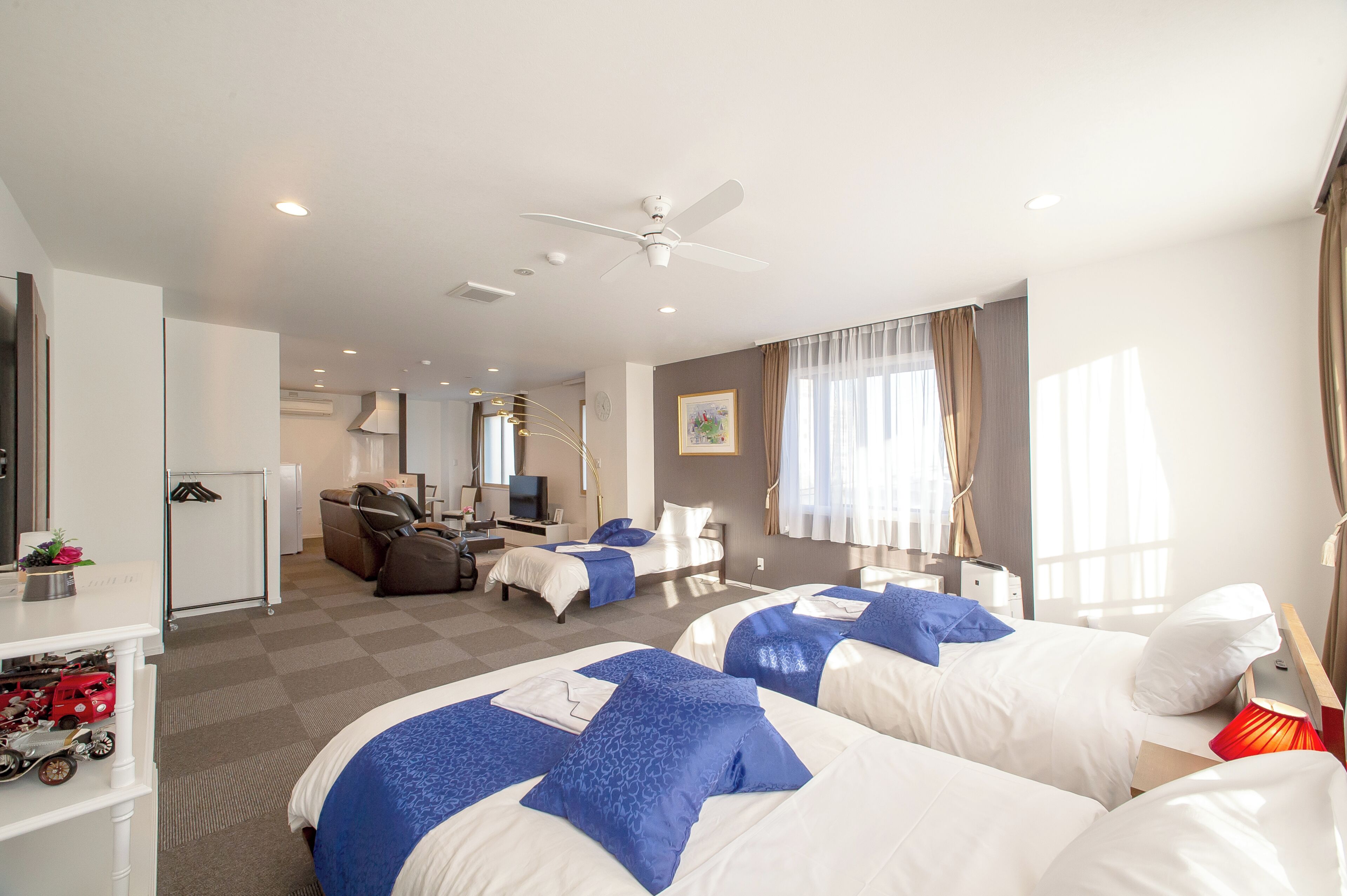 A hotel room with two beds, a desk, a chair, a TV, and a ceiling fan.