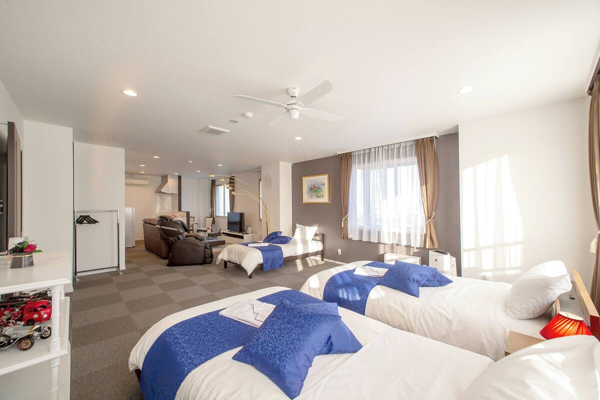 Habitación de hotel con dos camas, un escritorio, una silla, un televisor y un ventilador de techo.