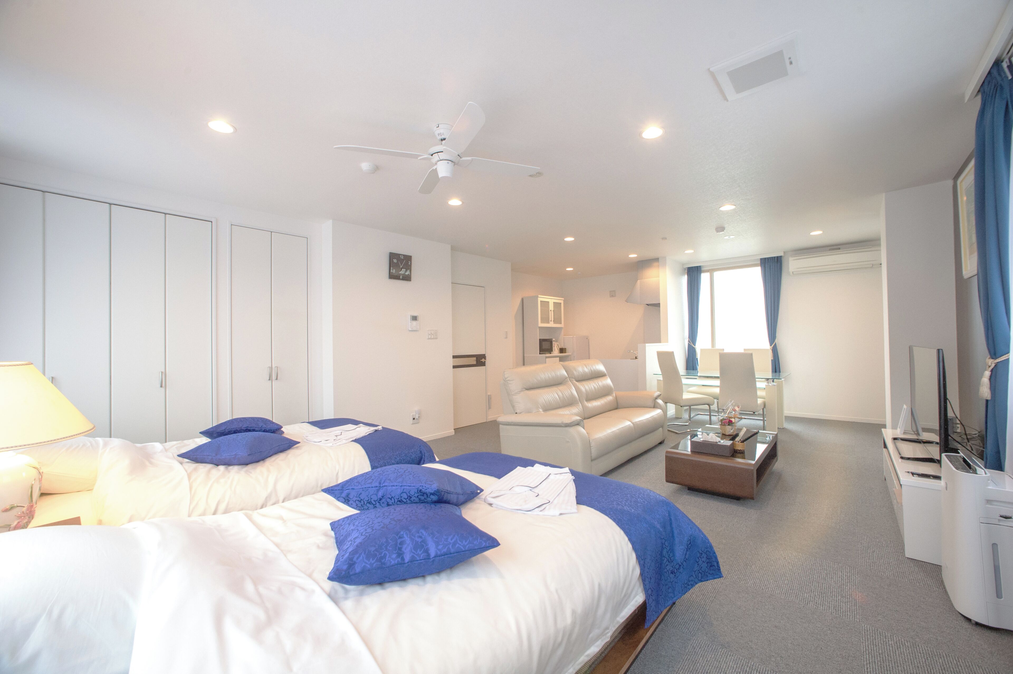 A hotel room with two beds, a sofa, a TV, and a ceiling fan.
