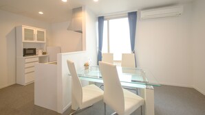 A modern, well-lit room with a glass dining table, white chairs, a microwave, and a kitchenette. - Condominium Panoramique Motomachi (Hakodate)