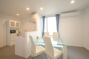 A modern room with a glass dining table, white chairs, a microwave, and a kitchenette. - Condominium Panoramique Motomachi (Hakodate)