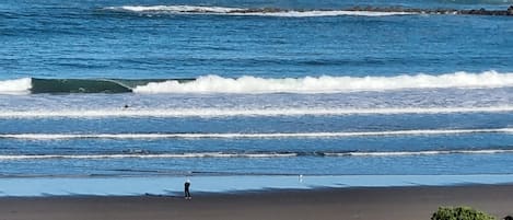 A beach with waves, a person standing, and some structures in the foreground.