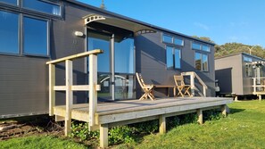 Una casa móvil moderna con una terraza, dos sillas de madera y un ventanal grande.