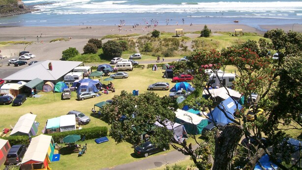 Un terrain de camping avec des tentes et des camping-cars, situé près d’une plage où l’on peut observer les vagues.
