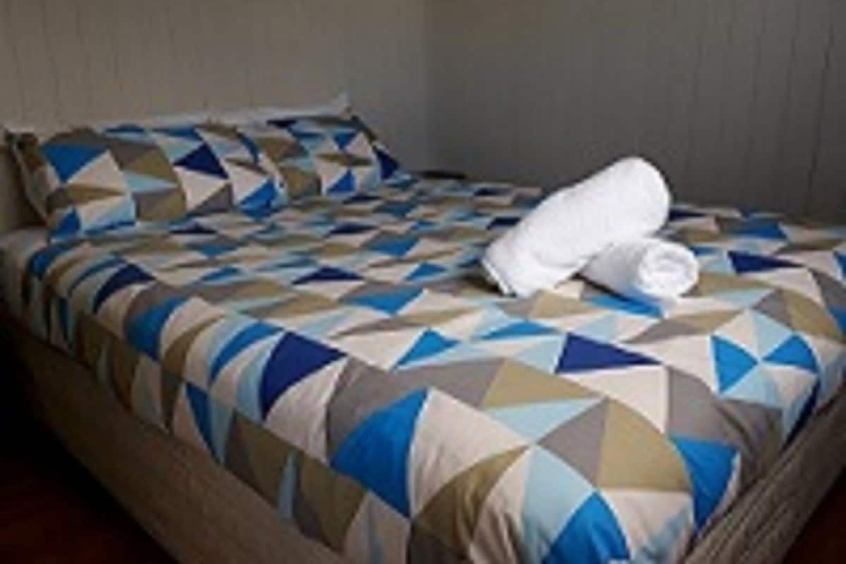 A bed with a geometric patterned bedspread, a white pillow, and a folded towel on the bed.