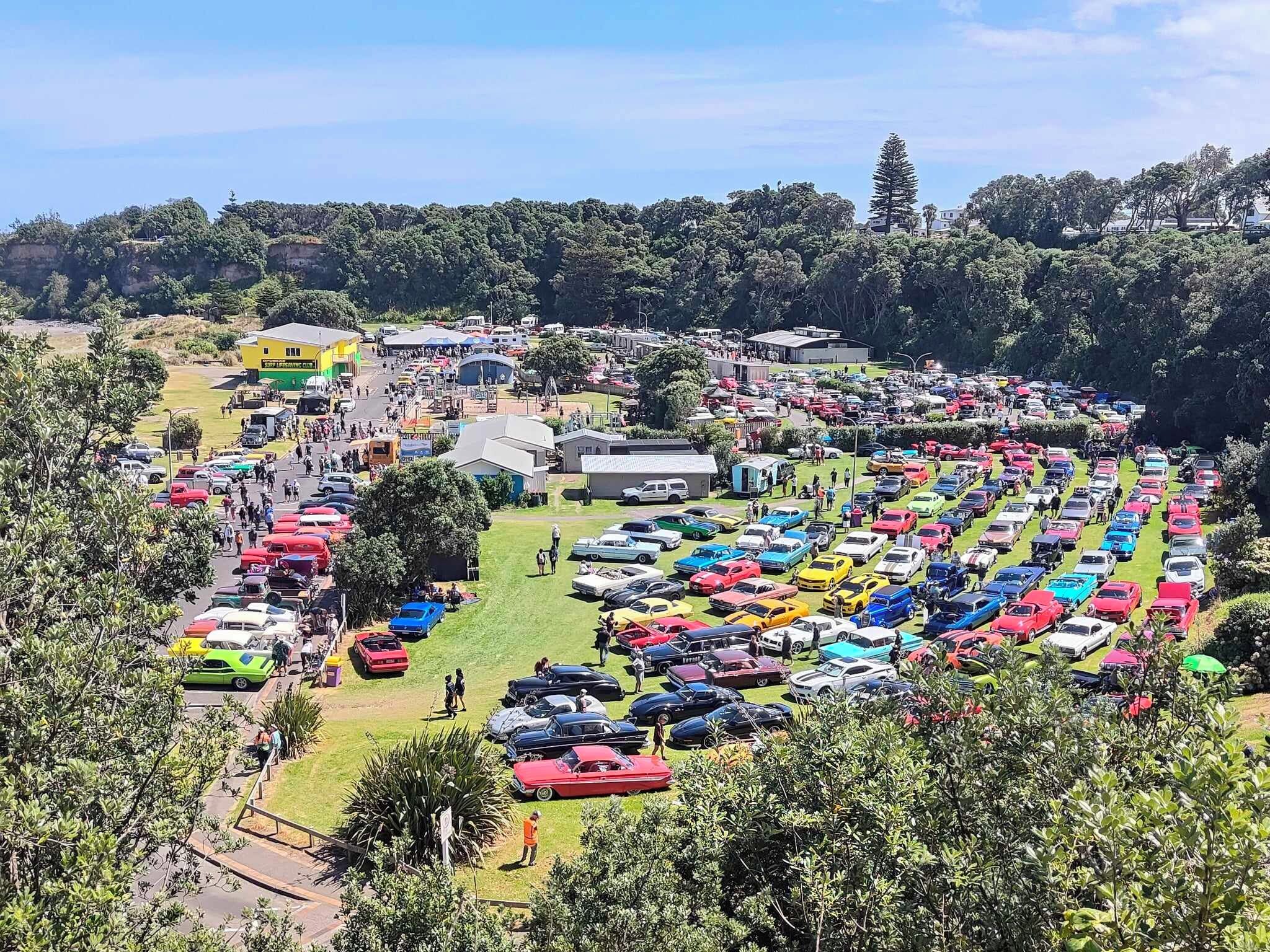 A large outdoor parking area with numerous parked cars and a few buildings in the background.