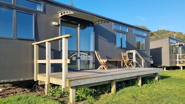 Una casa móvil moderna con terraza, dos sillas de madera y un gran ventanal corredero.