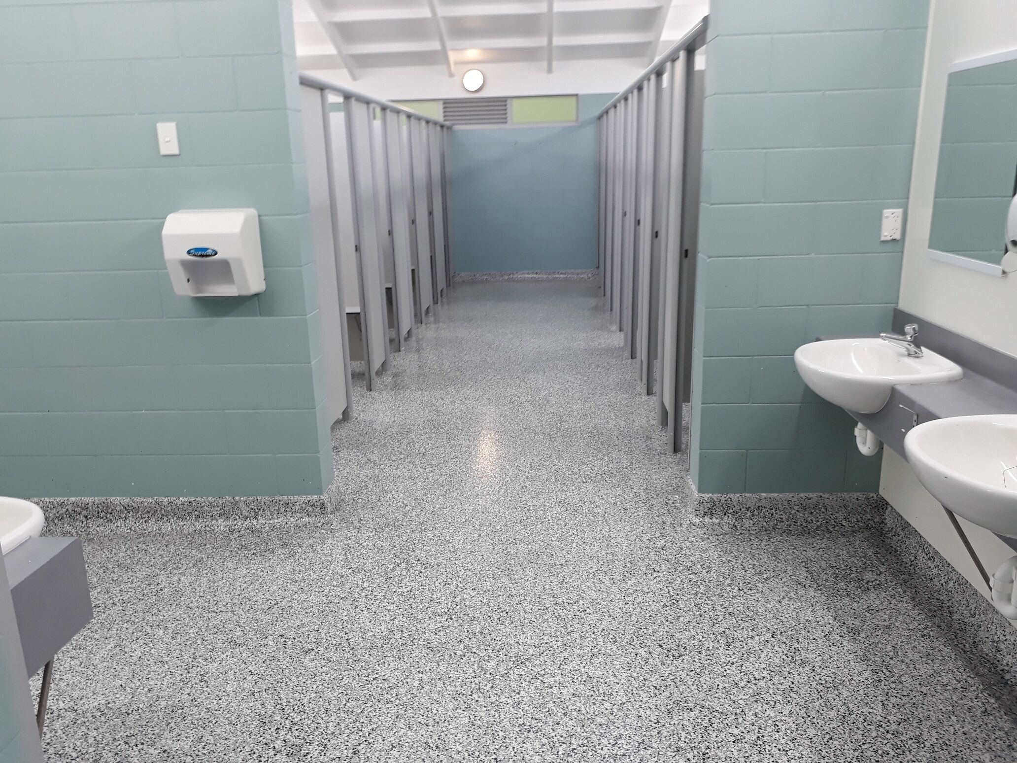 A public restroom with multiple stalls, a hand dryer, and two sinks.