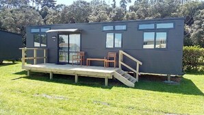 Une maison mobile moderne et compacte, dotée d’une petite terrasse, de deux chaises et d’un escalier menant à une porte.