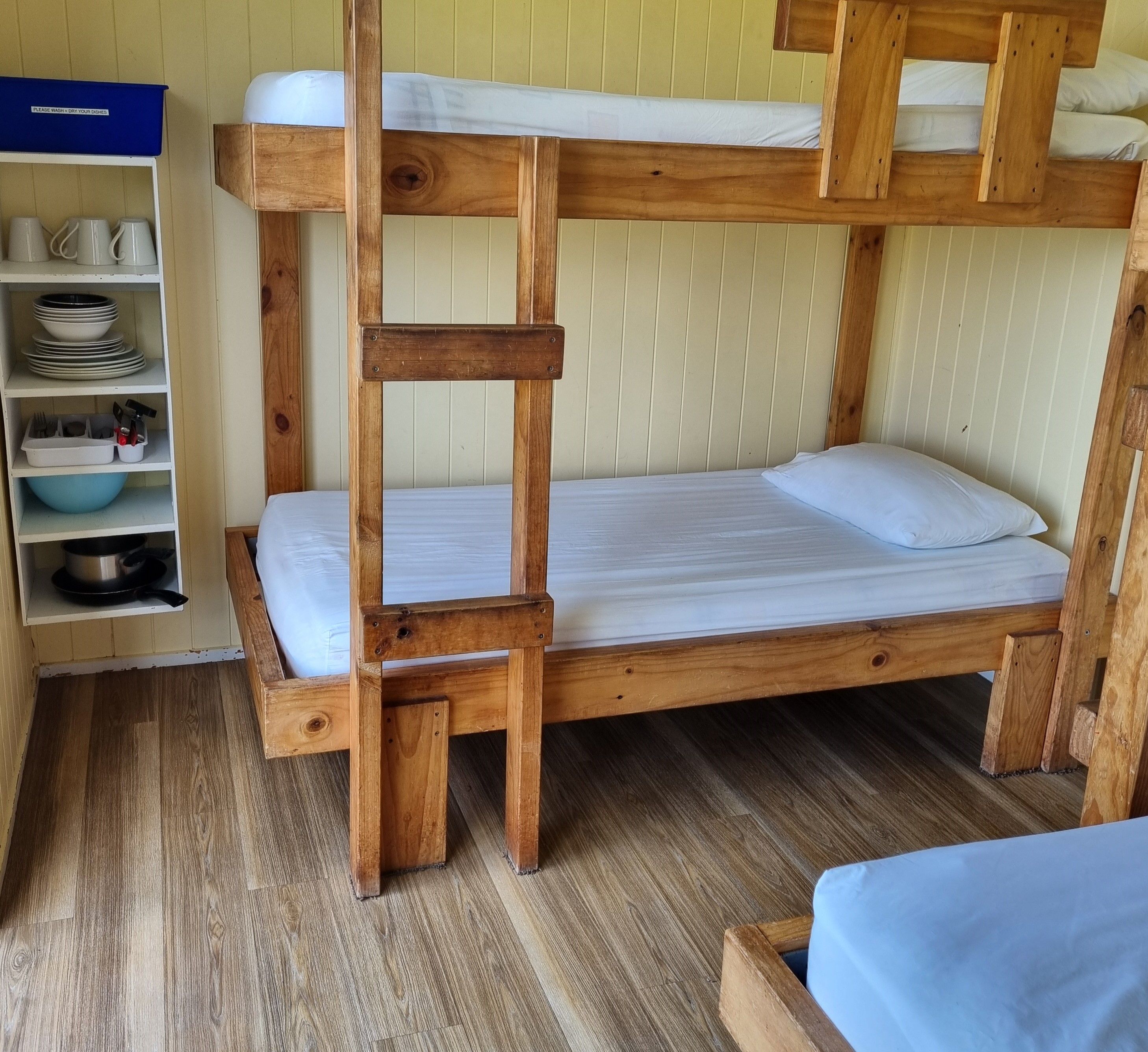 Una cama litera con una estantería a un lado que contiene platos y utensilios.