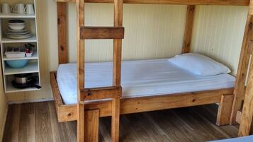 Una cama litera con una estantería a un lado que contiene platos y utensilios.