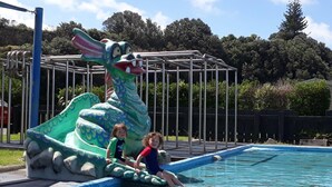 Une piscine avec un toboggan en forme de dragon, entourée de rampes métalliques et bordée d’arbres en arrière-plan.