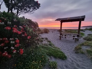 Une plage avec un kiosque en bois et des bancs, entourée de sable et de végétation.