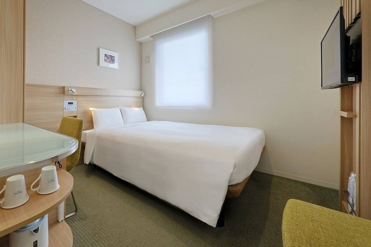 Habitación de hotel con cama, escritorio, computadora, silla y televisión.