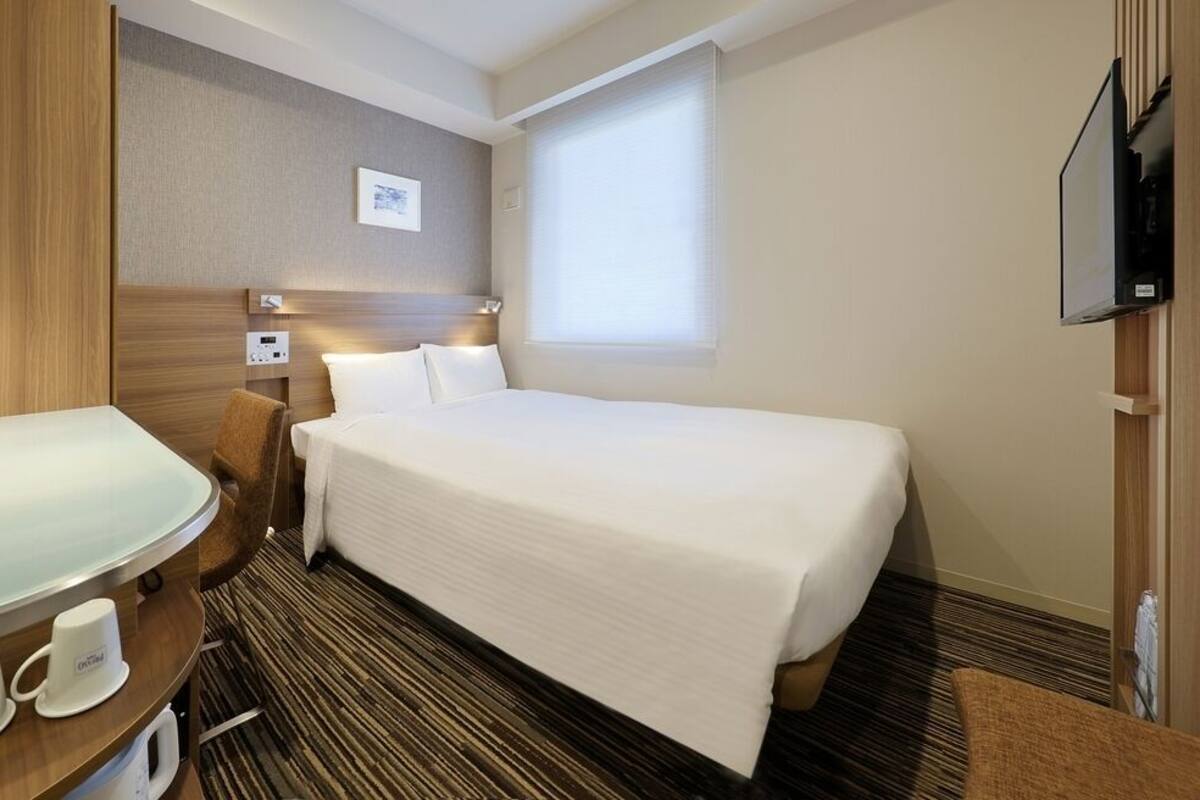 Una habitación de hotel con una cama, un escritorio con un teléfono y una taza, un televisor y una ventana.