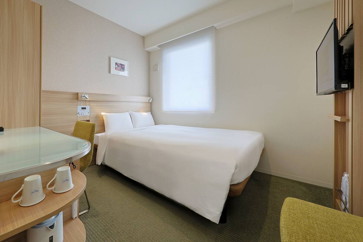 Una habitación de hotel con una cama, televisión, escritorio y silla, y una ventana.