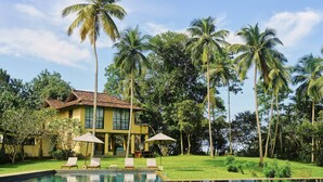A yellow building with a tiled roof, surrounded by a pool and palm trees. - Samadara Estate, Midigama (Ahangama)