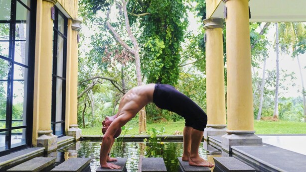A person performing a yoga pose on stone platforms by a water feature, with columns and greenery in the background. - Samadara Estate, Midigama (Ahangama)