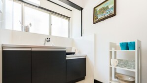 A modern kitchen with a black and white color scheme, a window above the sink, and a shelf with dishes and a kettle. - Otsu Ousaka House (Otsu)