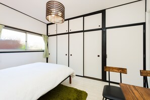 A bedroom with a bed, a green rug, a wooden chair, a table, and a wardrobe with sliding doors. - Otsu Ousaka House (Otsu)