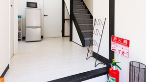 A modern interior with a staircase, a fire extinguisher, and a white refrigerator. - Otsu Ousaka House (Otsu)