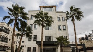 Un hotel de varios pisos con un diseño arquitectónico moderno, que cuenta con una entrada central con puertas de vidrio, rodeado de palmeras.