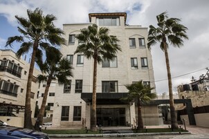 Un hotel de varios pisos con un diseño arquitectónico moderno, que cuenta con una entrada central con puertas de vidrio, rodeado de palmeras.
