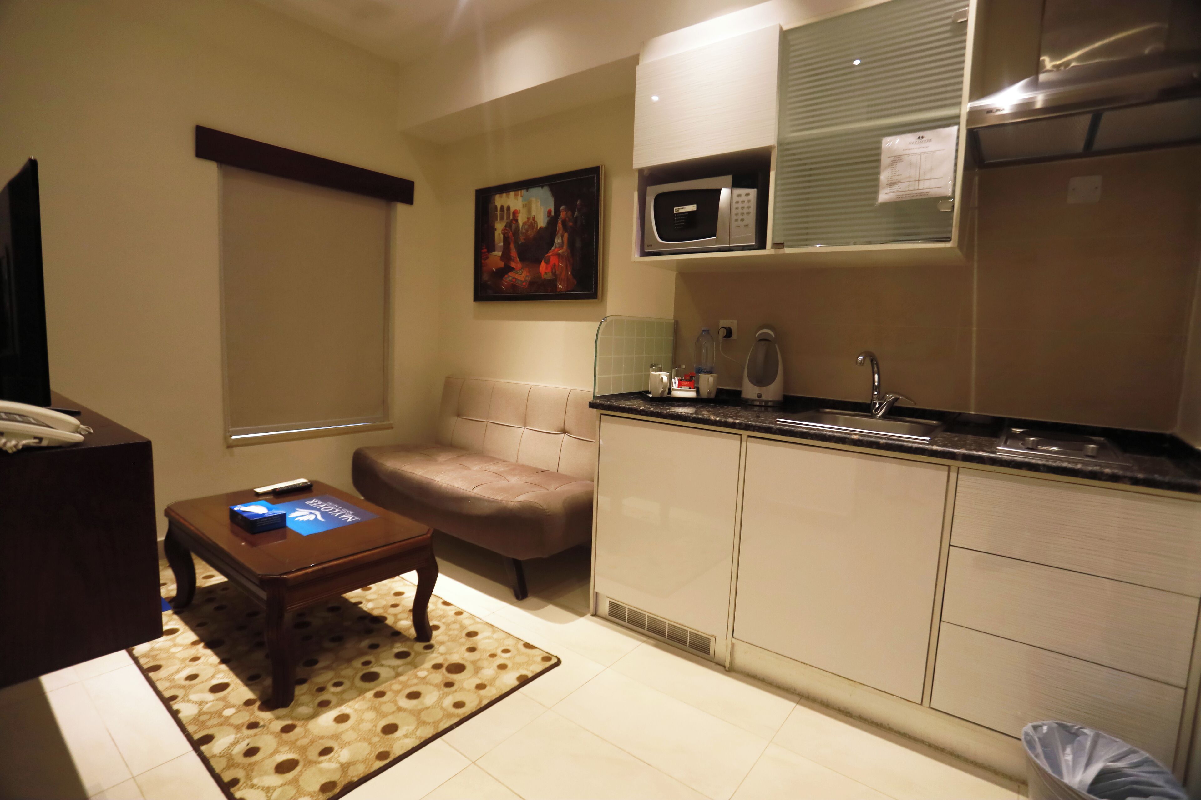 A compact living space with a kitchenette, a sofa, a coffee table, and a painting on the wall.