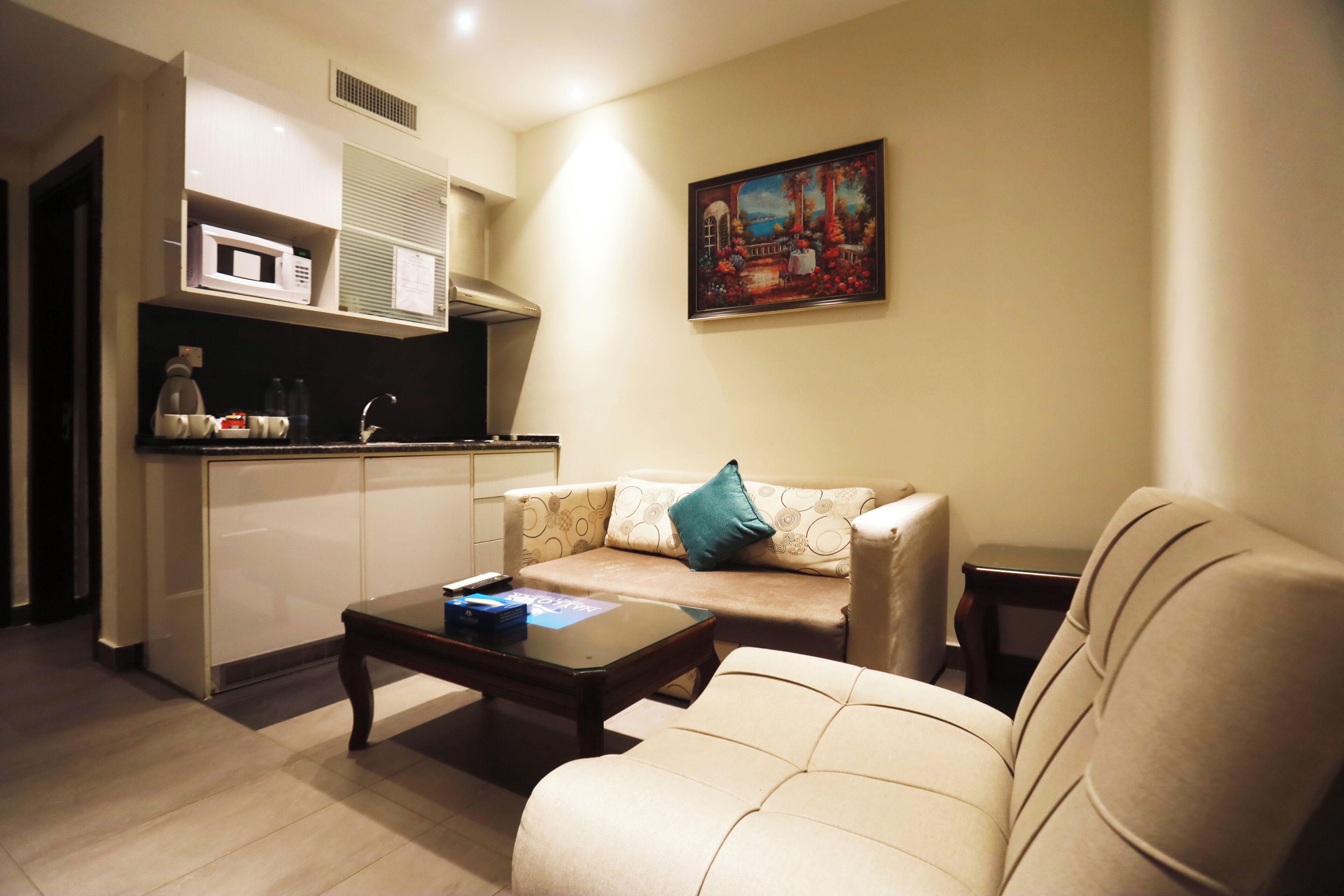 A living room with a sofa, a coffee table, and a kitchen area with a microwave.