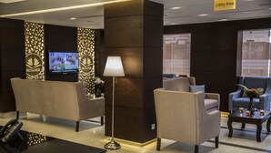 Un área de recepción con asientos, un televisor y una lámpara.