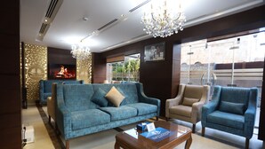 Un vestíbulo moderno con un sofá azul, sillones color beige, una mesa de centro de madera y una araña.