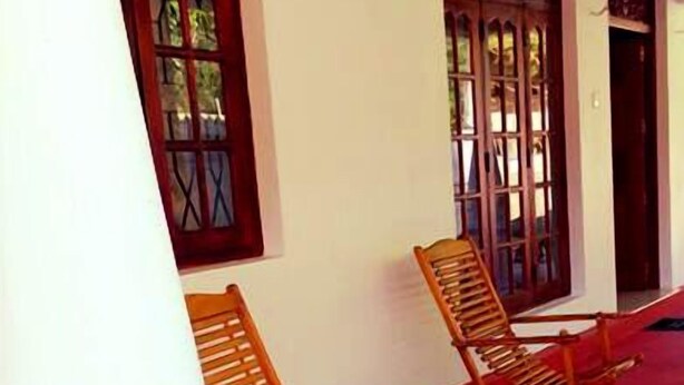 A covered outdoor area with two wooden rocking chairs and a red carpet. - Rockview Holiday Bungalow (Ukuwela)