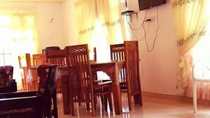 A spacious room with a tiled floor, a piano, wooden chairs, a dining table, and a TV mounted on the wall. - Rockview Holiday Bungalow (Ukuwela)