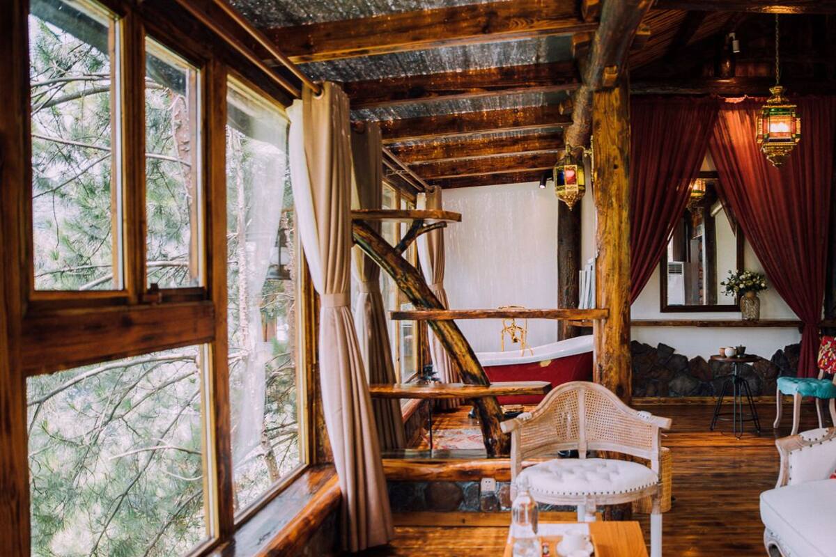 Een rustiek houten interieur met grote ramen, een houten trap en een zithoek met een tafel en stoelen.