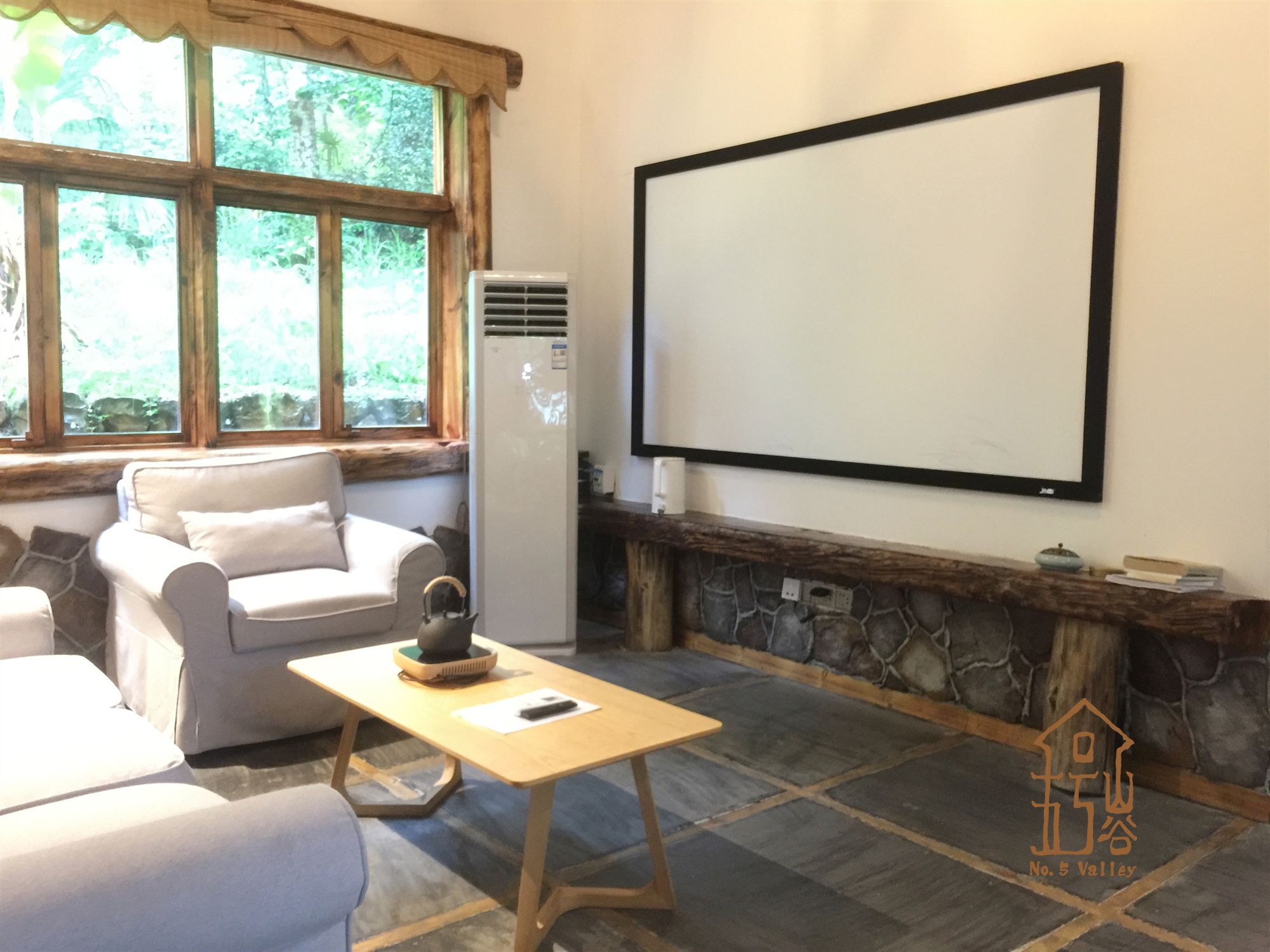 Ein Zimmer mit Kamin aus Stein, einem weißen Sofa, einem Holztisch und einer Projektionsleinwand an der Wand.