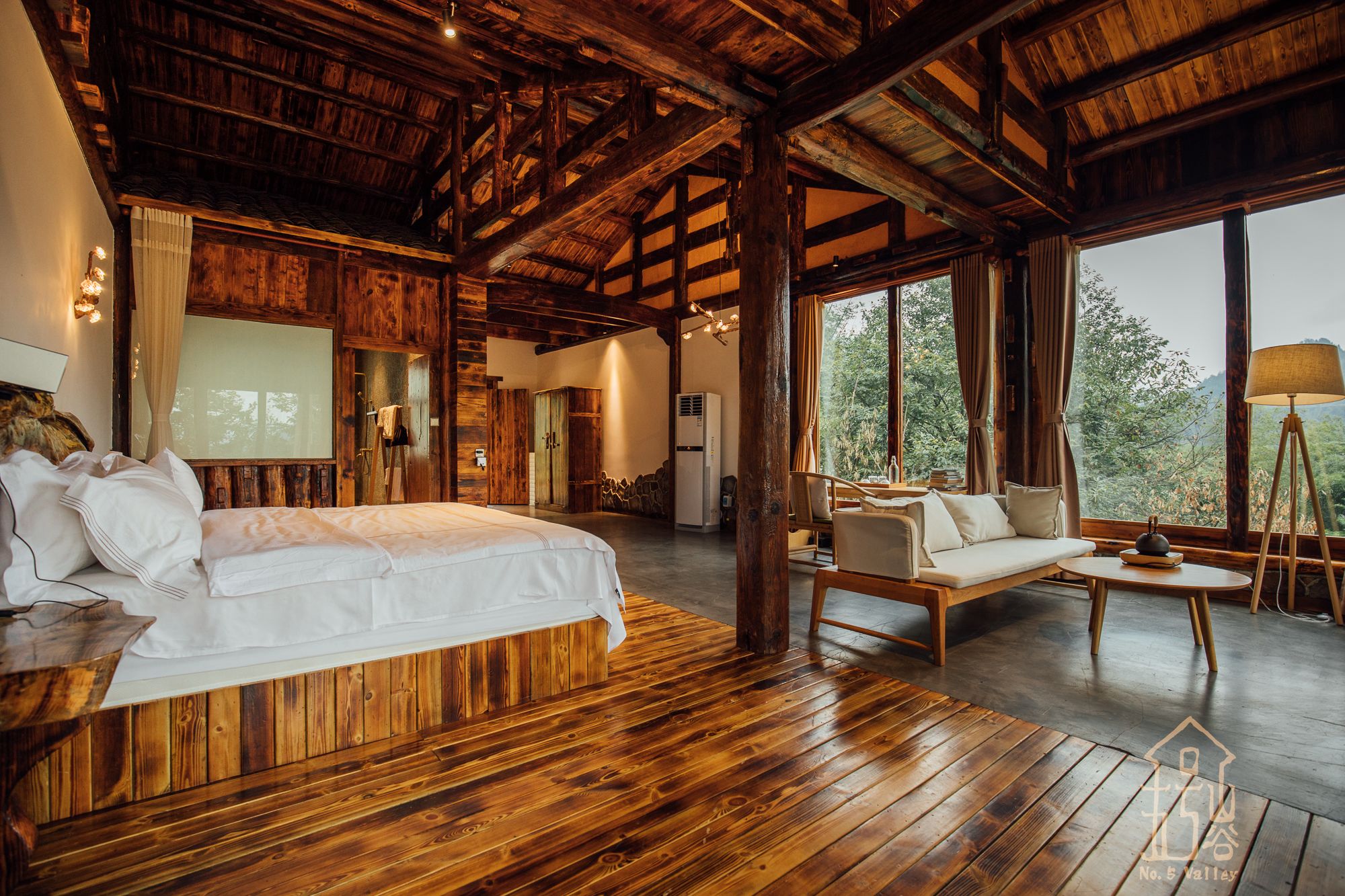 Une chambre spacieuse avec un grand lit, un canapé et une table à manger. De grandes fenêtres offrent une vue sur l’extérieur.