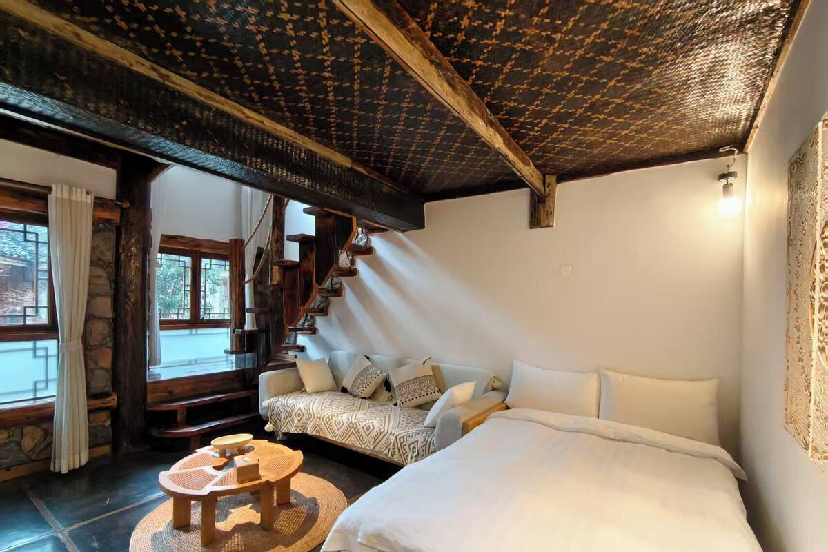 Een gezellige kamer met een bed, een bank, een kleine tafel en een trap naar een hoger gelegen verdieping.