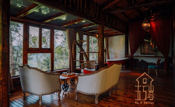 Un interior rústico con vigas de madera, un ventanal con vistas a árboles, una bañera antigua y un símbolo tradicional chino.