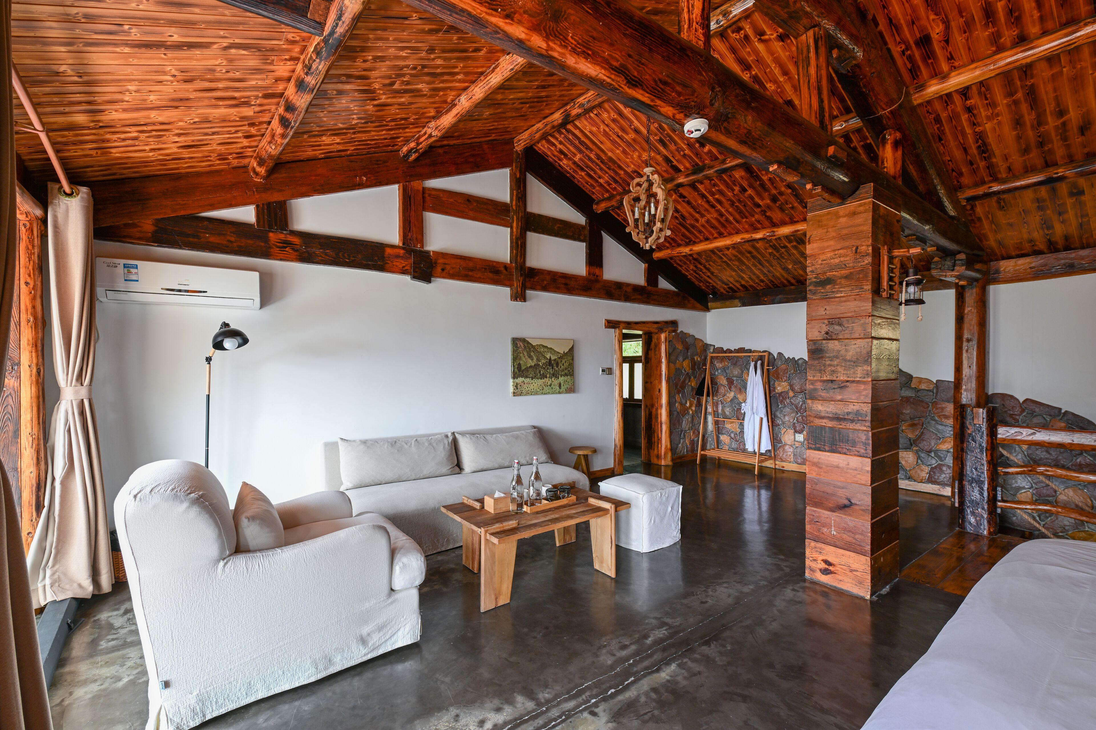 A spacious living area with a high wooden ceiling, a sofa set, a coffee table, and a stone wall.