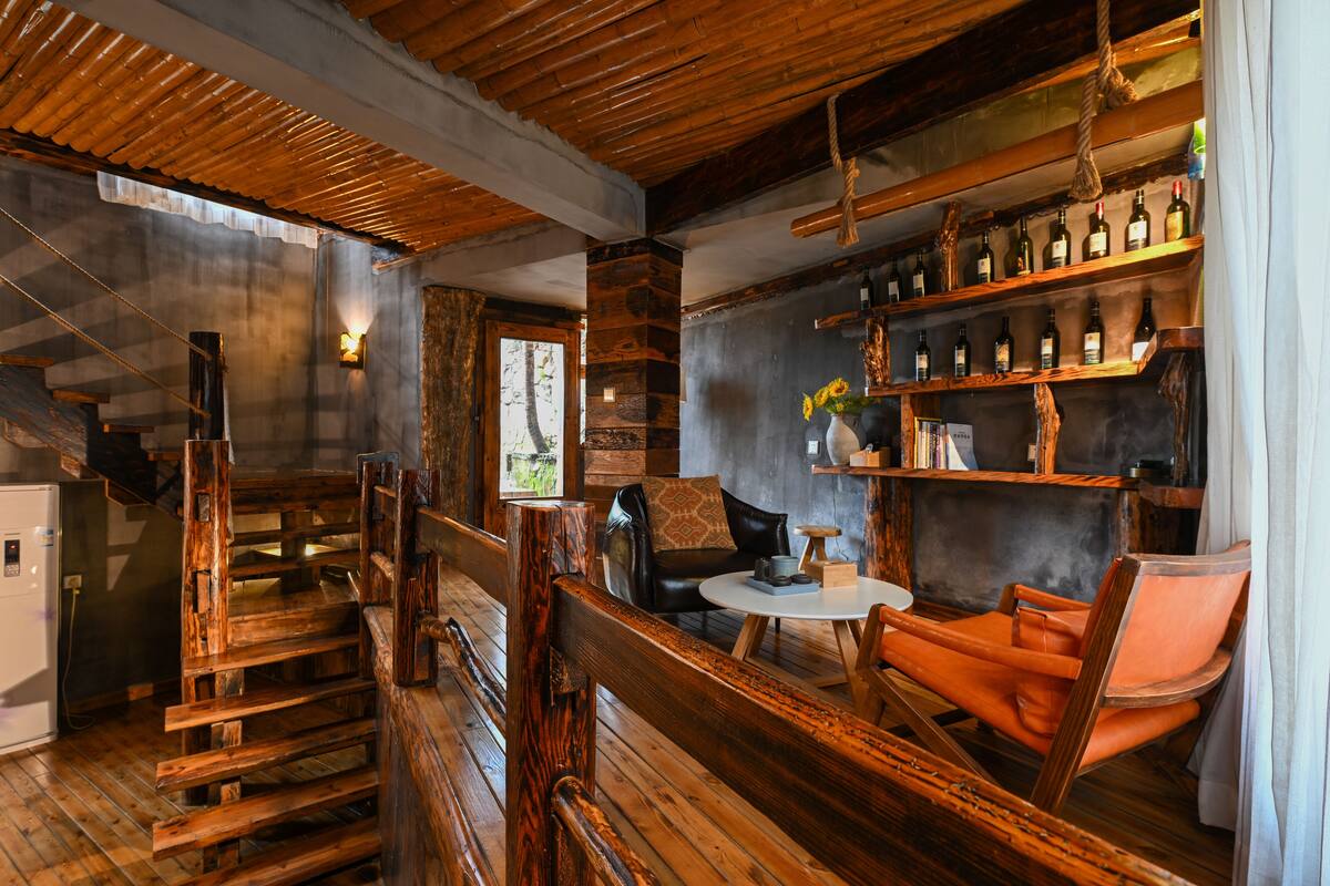 Een rustiek interieur met houten vloeren, een bar met flessenkasten, een zithoek met een tafel en stoelen, en een trap.