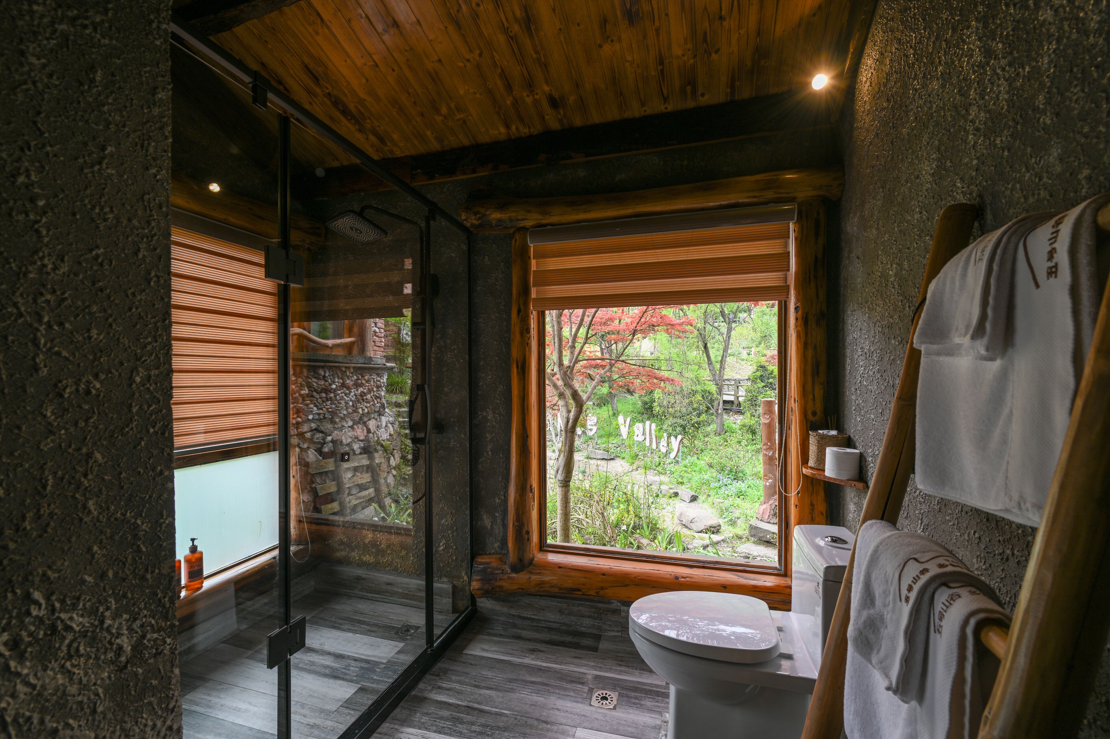 Un baño con techo de madera, inodoro, lavamanos y ventana con vistas a un jardín.